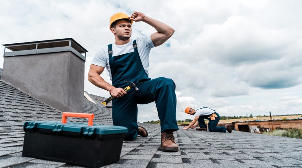 selective focus of handsome handyman touching helmet while holding hammer