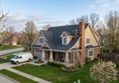 Aerial photo of a professional roofer wearing a harness to conduct a spring roof inspection in Westerville, OH, on a suburban home with blooming trees.
